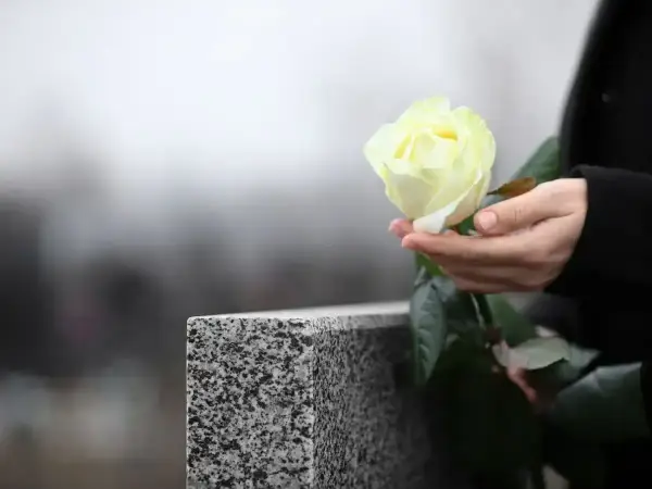Dłoń trzyma białą różę przy nagrobku. Pytanie, jak długo nie można ruszać rzeczy zmarłego, wciąż pozostaje.