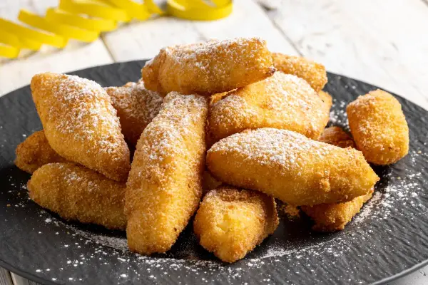 Un mucchio di dorate crema fritta, cosparse di zucchero a velo, su un piatto scuro.