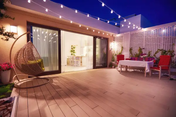 Terraza con silla colgante y mesa, iluminada por una guirnalda de luces. La pantalla lámpara plisada ilumina el ambiente.