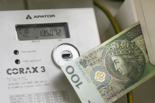 Licznik energii elektrycznej z banknotem 100 zł. Wysokie rachunki za prąd to problem, ale dodatek energetyczny może pomóc.