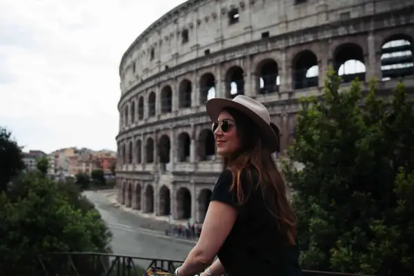 Une femme avec un chapeau et des lunettes de soleil admire le Colisée. Je visite Rome et ce moment est inoubliable.