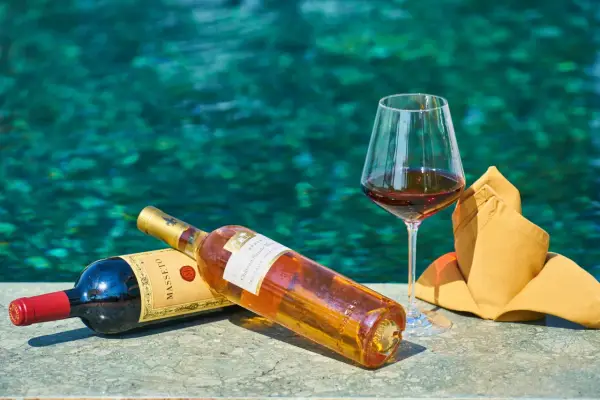 Due bottiglie di vino e un bicchiere pieno, con uno sfondo acquatico turchese. Un'immagine che evoca il sapido significato del relax e del piacere.