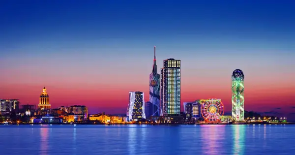 Widok na nowoczesną panoramę Batumi, stolicę Adżarii, o zachodzie słońca. Błyszczące wieżowce i diabelski młyn odbijają się w spokojnej wodzie.