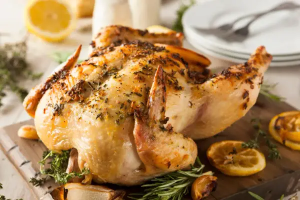 Un délicieux poulet à la broche, doré et savoureux, garni d'herbes fraîches et de quartiers de citron grillés sur une planche en bois.