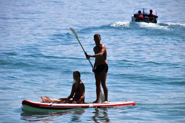 Ein Mann steht auf einem Stand Up Paddle Board auf dem Meer, während eine Frau sitzt. Im Hintergrund fährt ein Boot.