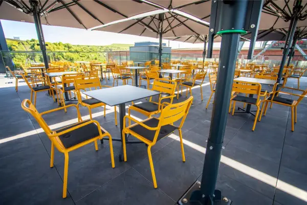 Leere gelbe Stühle und Tische unter Sonnenschirmen auf der Terrasse des Zeche Ewald Cafés.