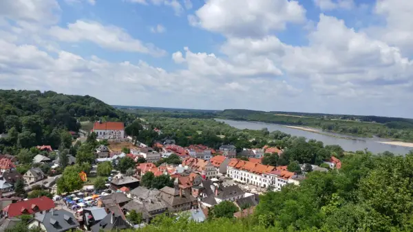 Widok na Kazimierz Dolny z górami Trzech Krzyży w tle. Rzeka Wisła, zielone wzgórza i urokliwe miasteczko z czerwonymi dachami.
