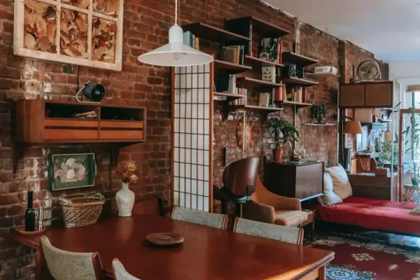 Wnętrze kawalerki z ceglaną ścianą, drewnianym stołem i meblami w stylu vintage.