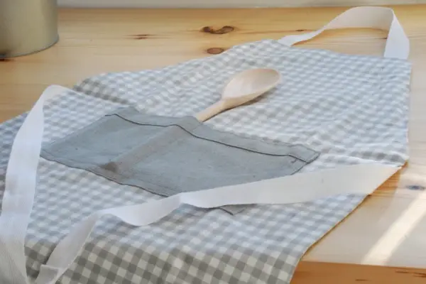 Gotowy fartuch kuchenny w kratkę, z drewnianą łyżką w kieszeni. Idealny poradnik, jak uszyć fartuch kuchenny.