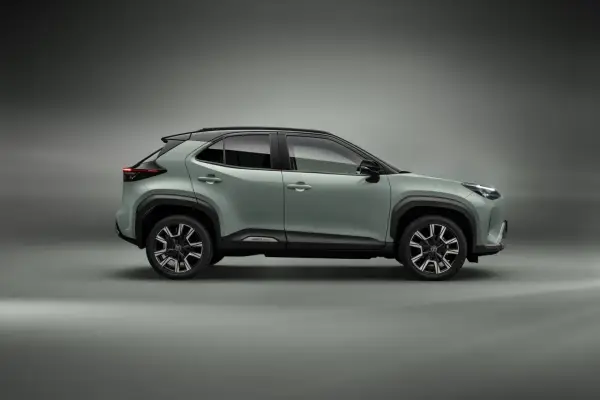 Nowy, zielony toyota crossover Yaris Cross z czarnym dachem i felgami stoi na szarym tle.
