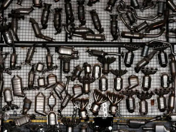 Duża kolekcja metalowych części samochodowych, głównie katalizatorów, wiszących na siatce.