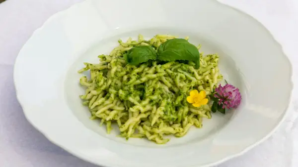 Pasta al pesto con hojas de albahaca fresca y flores comestibles.