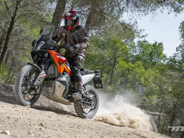 Motociclista con casco y equipo de aventura, derrapando una KTM 490 Adventure en un camino de tierra con polvo levantándose.