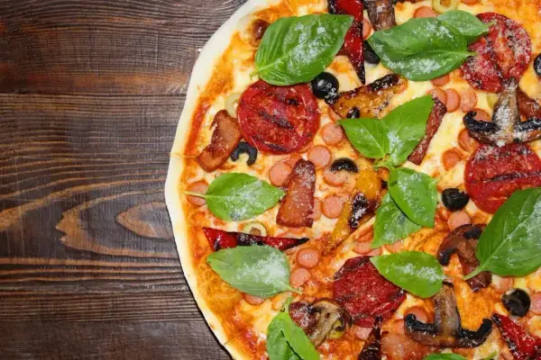 Pyszne rodzaje pizzy: z kiełbaską, boczkiem, pomidorami, oliwkami i bazylią na drewnianym tle.