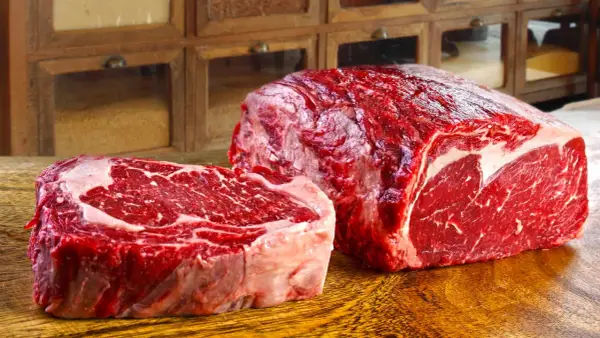 Deux pièces de viande rouge vif, un steak épais et un rôti, sur une planche en bois. Ce filet de bœuf promet un repas savoureux.