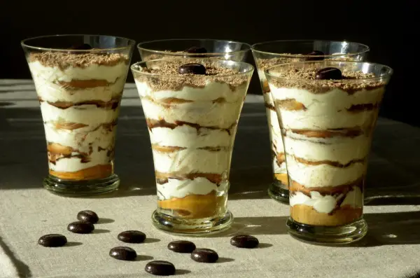 Pyszne tiramisu w pucharkach, warstwowo ułożone z kremem i biszkoptami, posypane czekoladą i kawą.