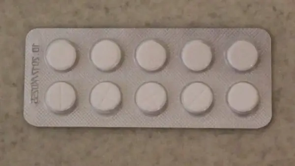 Opakowanie z dziesięcioma białymi tabletkami, niektóre z nacięciem. Może to być lek na receptę, np. tizagelan.