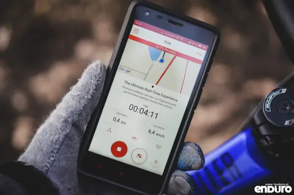 Rękawiczka trzyma smartfon z aplikacją licznik rowerowy. Widoczny czas 00:04:11, dystans 0,4 km i średnia prędkość 6,4 km/h.