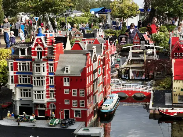 Miniaturowa holenderska zabudowa z kanałami i mostami w **Lego Land**. Ludzie spacerują wśród kolorowych budynków z klocków.