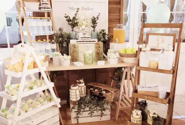 Un candy bar rústico con dulces, botellas de agua y un cartel "Mesa Dulce".