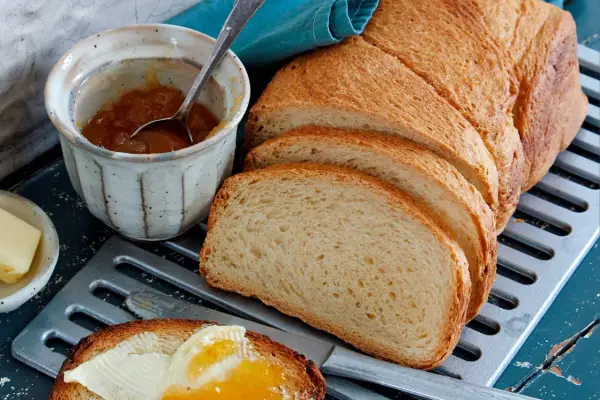 Ein Laib **sauerteig Toastbrot** ist aufgeschnitten. Daneben stehen Marmelade, Butter und ein Messer mit einem Stück Brot, das bestrichen ist.