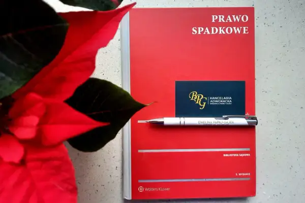 Czerwona książka "Prawo spadkowe" obok poinsecji. Długopis z nazwiskiem adwokatki i wizytówka kancelarii sugerują tematykę prawną, być może związaną z zapisem windykacyjnym.
