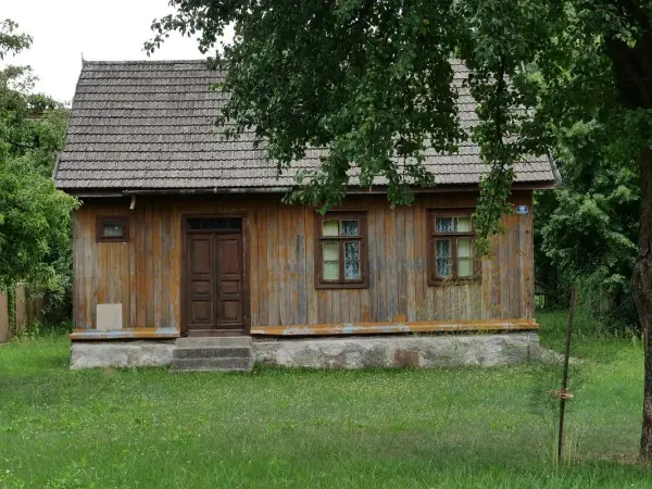 Drewniany dom z gontowym dachem, otoczony zielenią. Widać tu, kiedy dom jest zabytkiem, z jego wiekową, ale wciąż piękną fasadą.