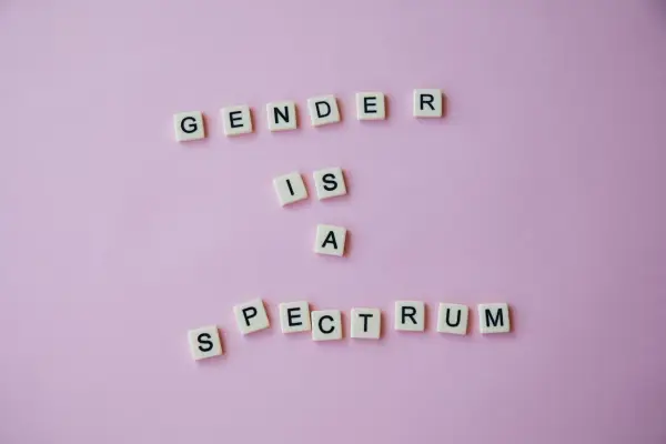 Litery na różowym tle układają się w napis "GENDER IS A SPECTRUM". To przypomnienie, że tożsamość płciowa nie jest binarna, a doświadczenie dysforii płciowej jest częścią tej złożoności.