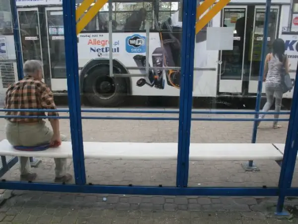 Mężczyzna czeka na przystanku na autobus 102. Rozkład jazdy jest niewidoczny, ale widać autobus z reklamą Allegro.