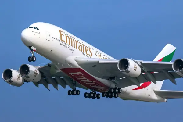 Ogromny Airbus A380 800 linii Emirates z wysuniętym podwoziem wznosi się na tle błękitnego nieba.