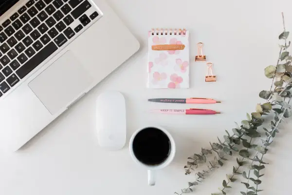 Ein Schreibtisch mit Laptop, Maus, Notizbuch, Stiften und Kaffee. Ideal für Lehrer, die ihr Zeitmanagement verbessern wollen.