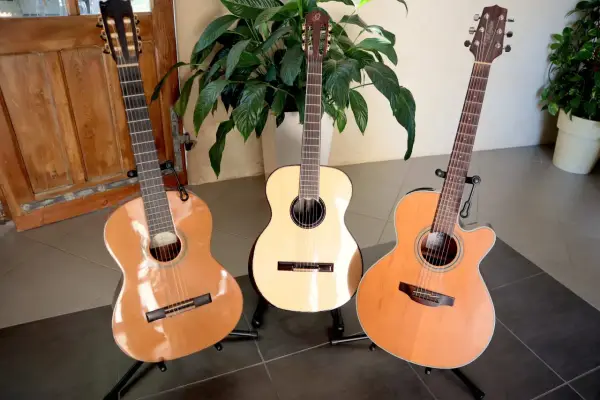 Trois guitares folk nylon, une classique, une électro-acoustique et une autre, se tiennent fièrement sur leurs supports, prêtes à faire vibrer leurs cordes.