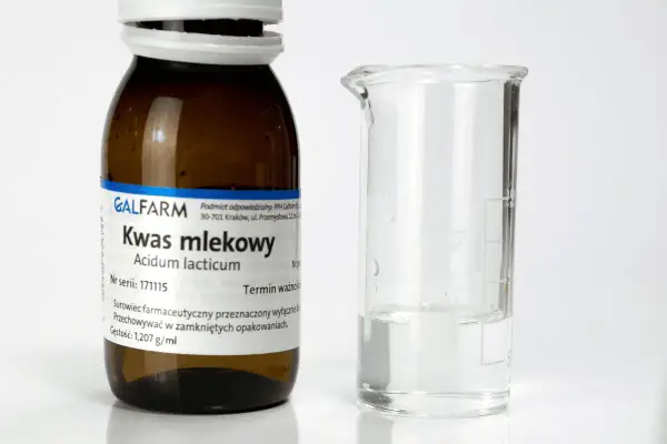 Butelka z napisem "Kwas mlekowy" i zlewka z płynem. Czy kwas mlekowy jest szkodliwy? Zależy od stężenia i zastosowania.