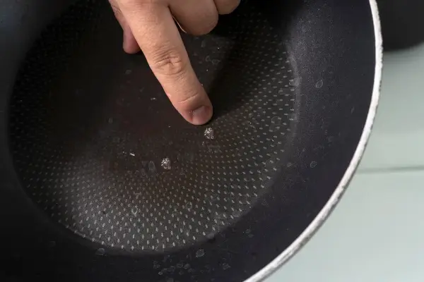 Palec wskazujący na uszkodzoną powłokę patelni. Czas na recykling i pytanie: gdzie wyrzucić patelnię?