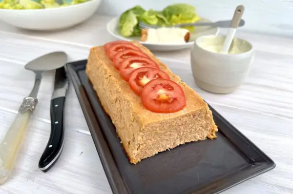 Un pain de thon savoureux, garni de rondelles de tomate fraîche, prêt à être dégusté avec une salade verte et une sauce crémeuse.