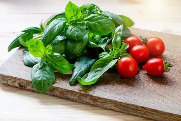 Un fascio di basilico fresco e pomodorini ciliegino su un tagliere di legno. La luce del sole illumina il basilico, creando un'esposizione perfetta per un'insalata estiva.