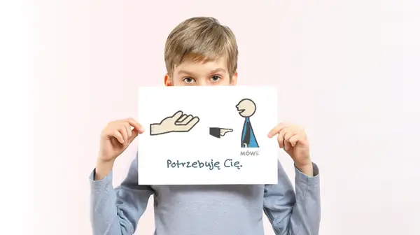 Chłopiec trzyma tabliczkę z rysunkiem dłoni, postaci i napisem "Potrzebuję Cię".