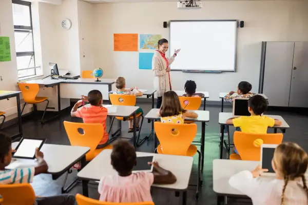 Nauczycielka prowadzi lekcję w klasie pełnej dzieci. To idealne miejsce do nauki pedagogiki przedszkolnej i wczesnoszkolnej w Poznaniu.