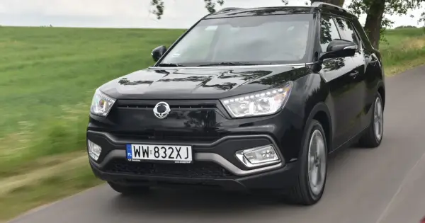 Czarny SsangYong Tivoli, model suw 2000, pędzi po wiejskiej drodze wśród zielonych pól.
