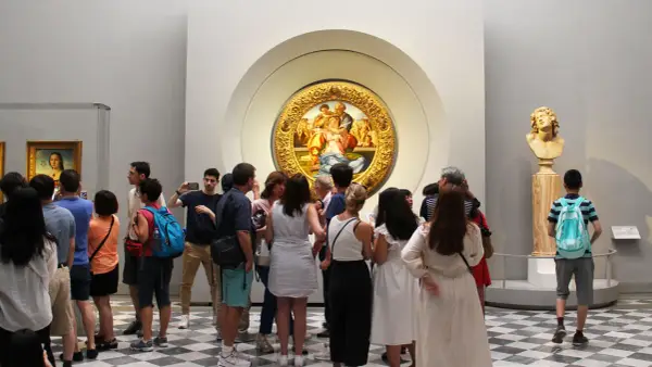 Galeria Uffizi: co zobaczyć? Grupa turystów podziwia okrągły obraz w złotej ramie i rzeźbę.