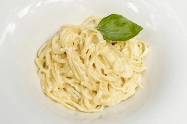 Un plato de spaghetti a la carbonara con nata, cremoso y adornado con una hoja de albahaca fresca.