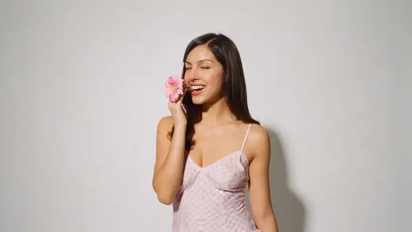 Olivia Rodrigo z różową gerberą w ustach, w różowej sukience w kratkę. Idealna na koncerty!