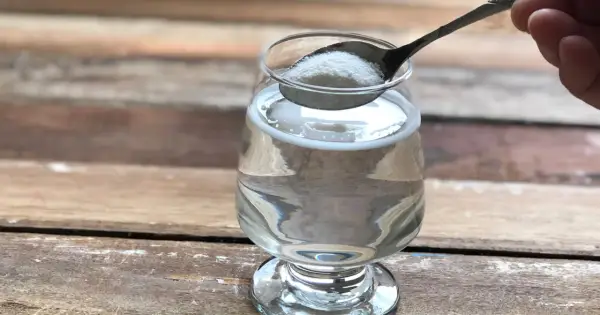 Łyżeczka z proszkiem, który może być naturalny kolagen na stawy, wsypywana do szklanki z wodą.