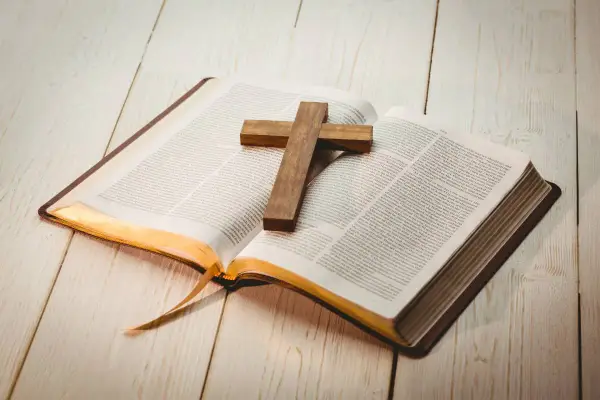 Otwarta Biblia z drewnianym krzyżem na stronach. Znajdź motywujące cytaty biblijne, które dodadzą Ci sił i nadziei.