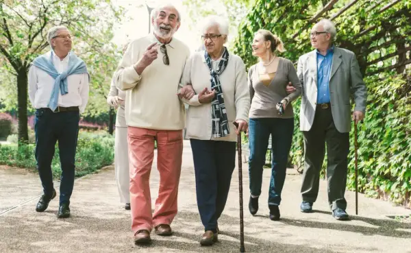 Grupa seniorów spaceruje po parku, ciesząc się świeżym powietrzem. Może rozmawiają o tym, jak przyjemnie jest płacić opłatę klimatyczną za takie widoki.
