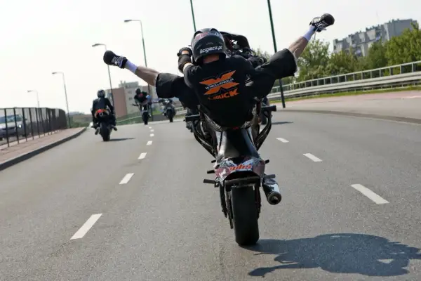 Motocyklista wykonuje jazdę na jednym kole z nogami w powietrzu. Ryzykowne wyczyny mogą skończyć się mandatem.