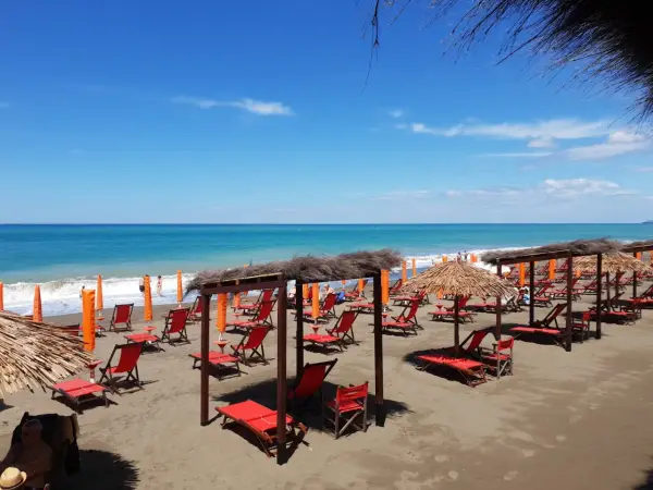 Plage de Marina di Bibbona avec des chaises longues rouges et des parasols de paille sous un ciel bleu éclatant.