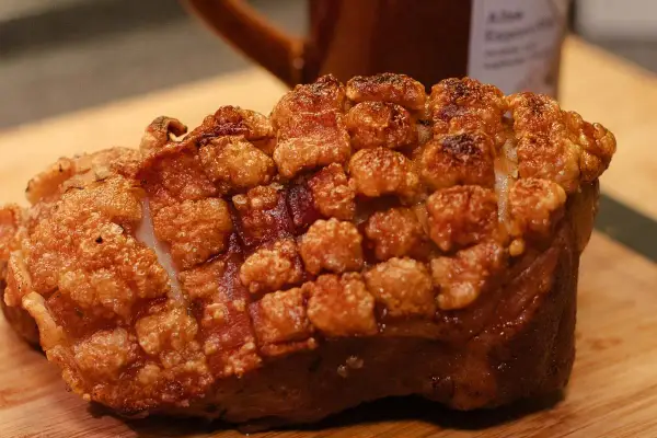 Ein knuspriger, ofenfrischer Schweinebraten mit goldbrauner Kruste liegt auf einem Holzbrett.