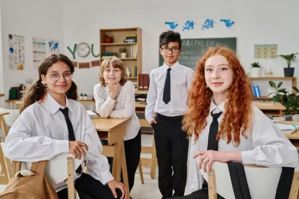 Vier Schüler in weißem Hemd und schwarzer Krawatte im Klassenzimmer. Ein Vergleich des Schulsystems Finnland und Deutschland könnte hier beginnen.
