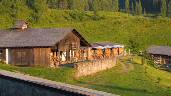 Malghe Alto Adige immerse nel verde, con rustici in legno e tavoli all'aperto sotto ombrelloni bianchi. Un'oasi di pace tra i boschi.